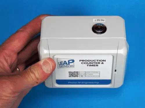 hand holding production counter timer wireless sensor showing top view reset button by Leap Sensors