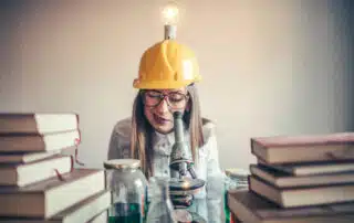 Woman wearing a hat with a light bulb looking into a microscope