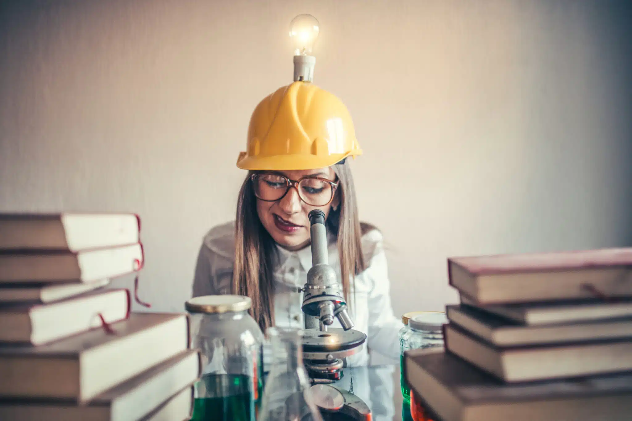 Woman wearing a hat with a light bulb looking into a microscope