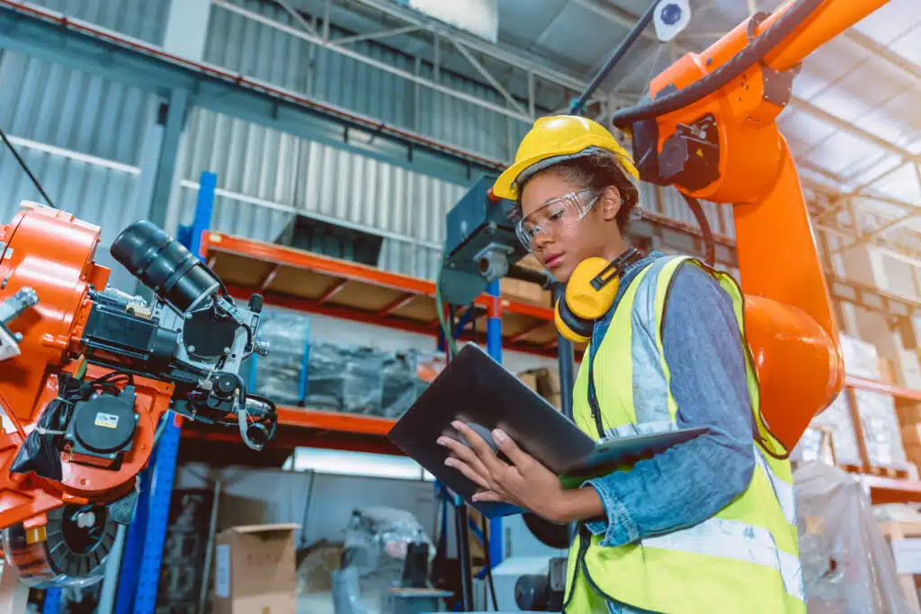 Engineer smart woman worker working programing robotic welding machine. Black teen girl work in advance modern factory.