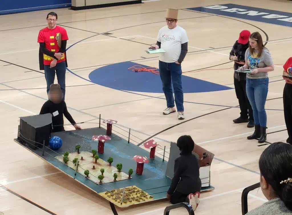 Students operating a large mock pinball machine while appraisers observe