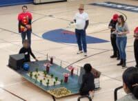 Students operating a large mock pinball machine while appraisers observe